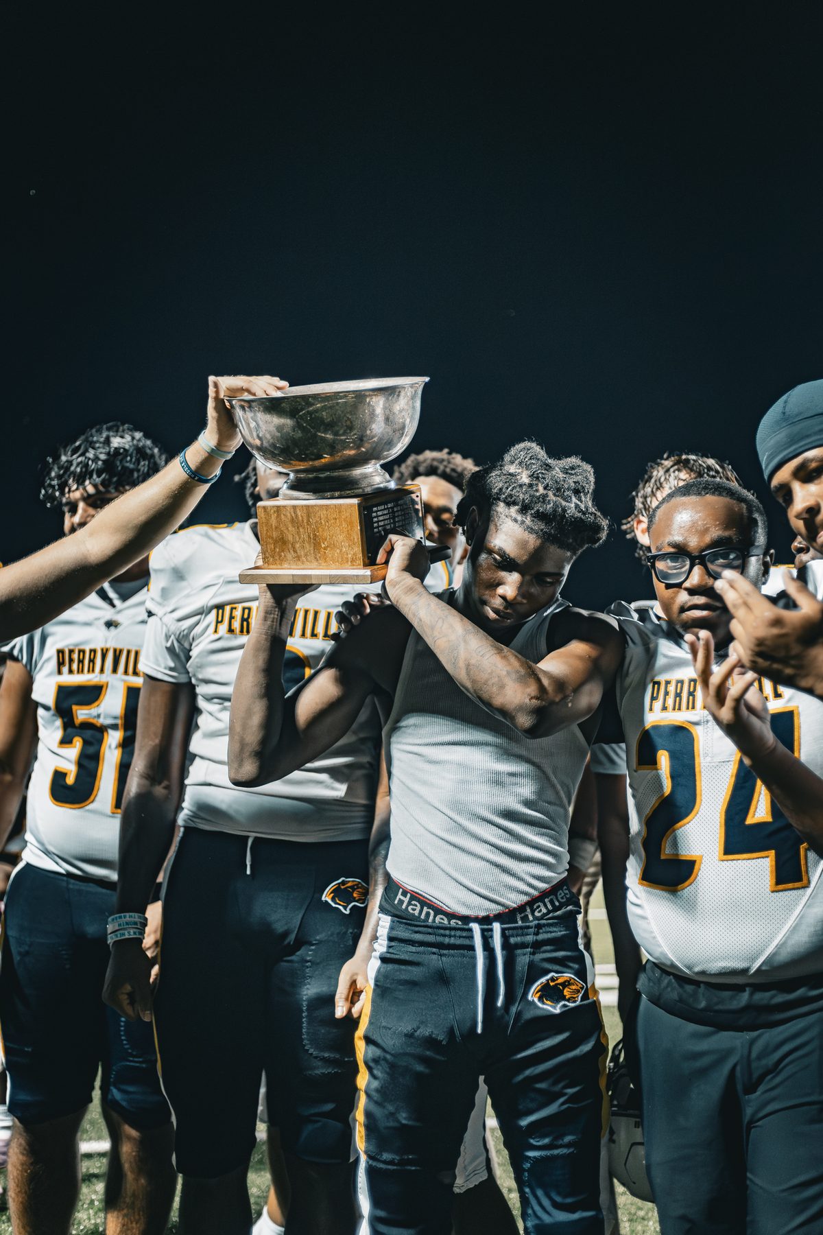 Football team celebrating a win under stadium lights as teammates hold a trophy overhead