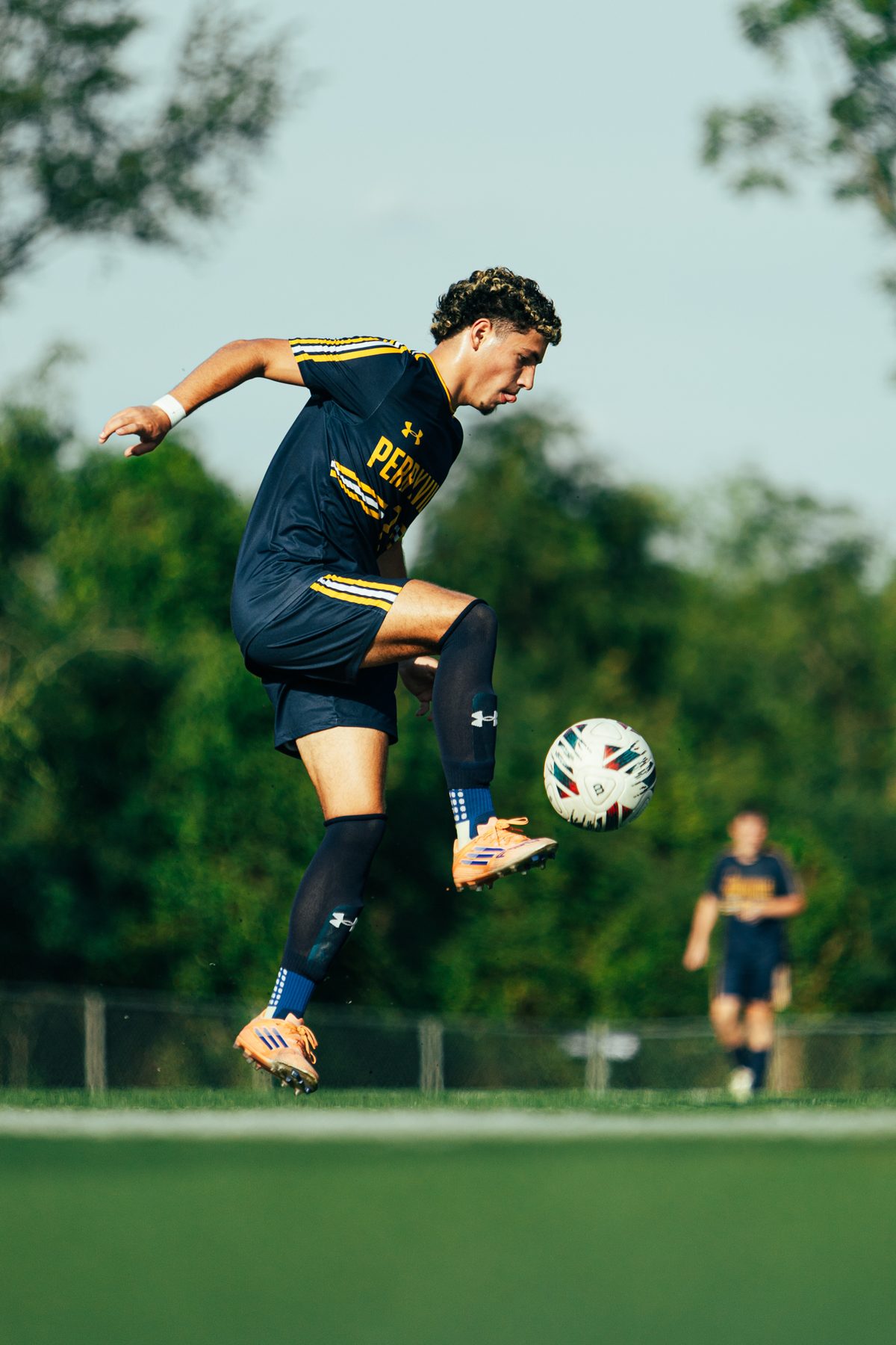Soccer player leaping off the ground to strike the ball out of the air in golden evening light