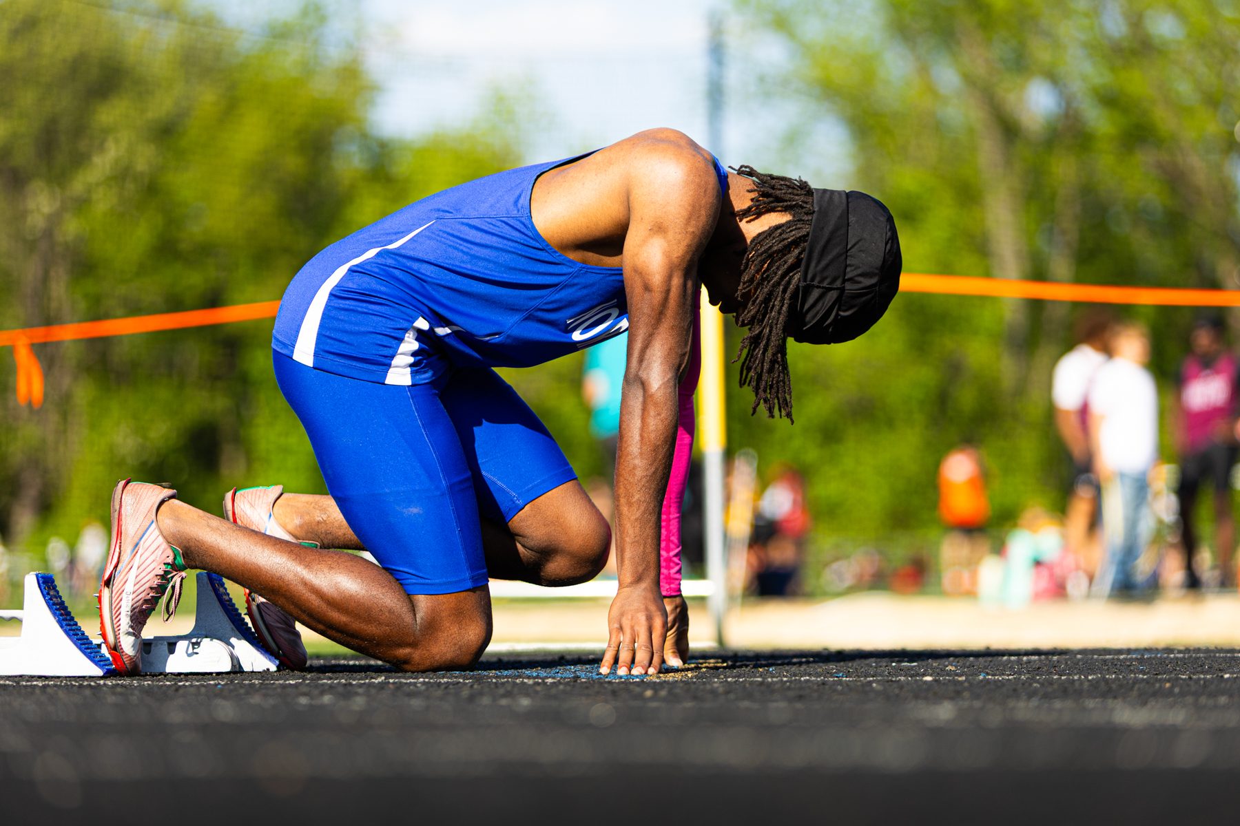Sprinter in a blue uniform down on one knee in the starting blocks with fingers on the line