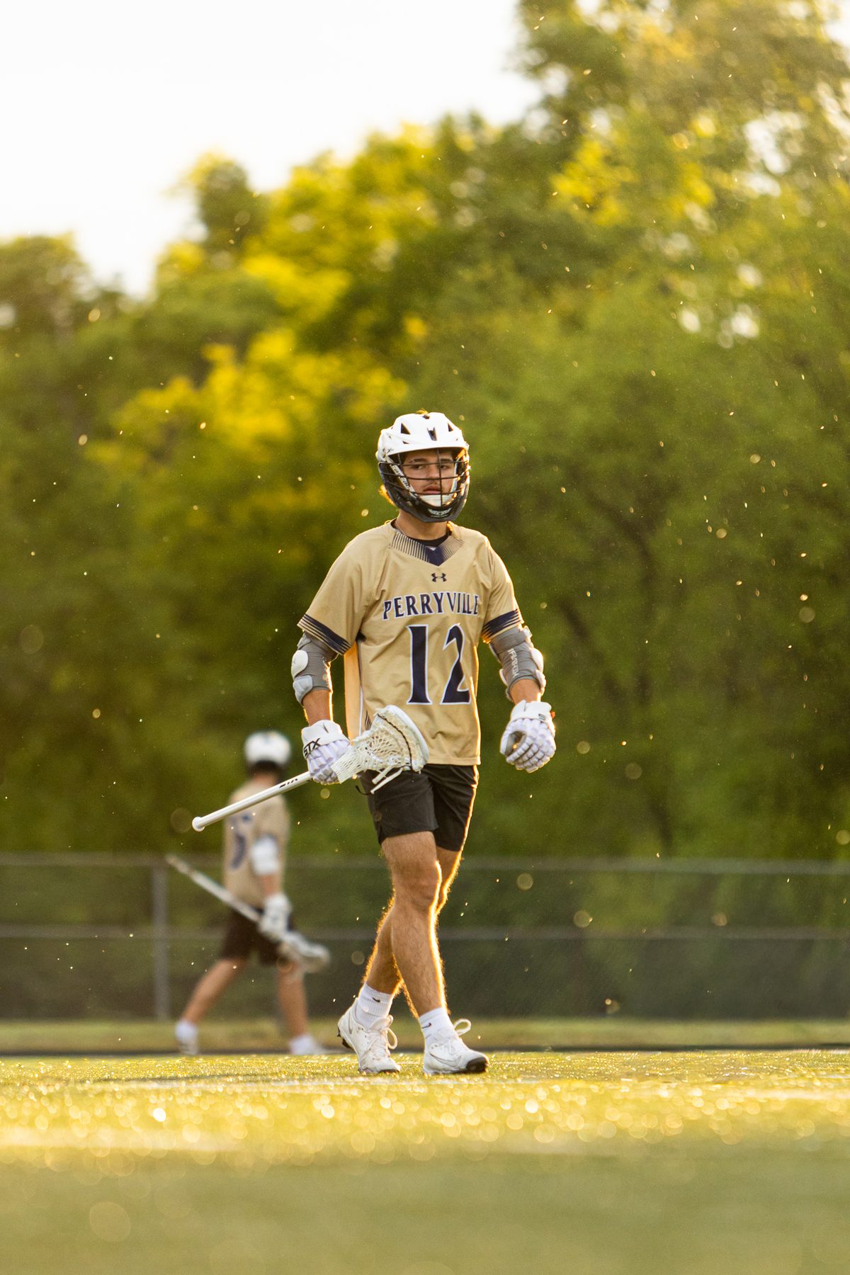 Lacrosse player number 12 walking up the field in warm golden hour light with pollen floating in the air